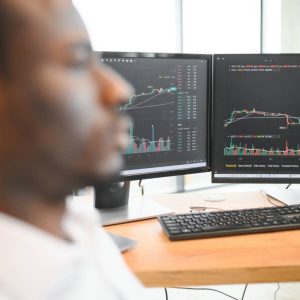 African-American broker works in office using workstation and analysis technology.